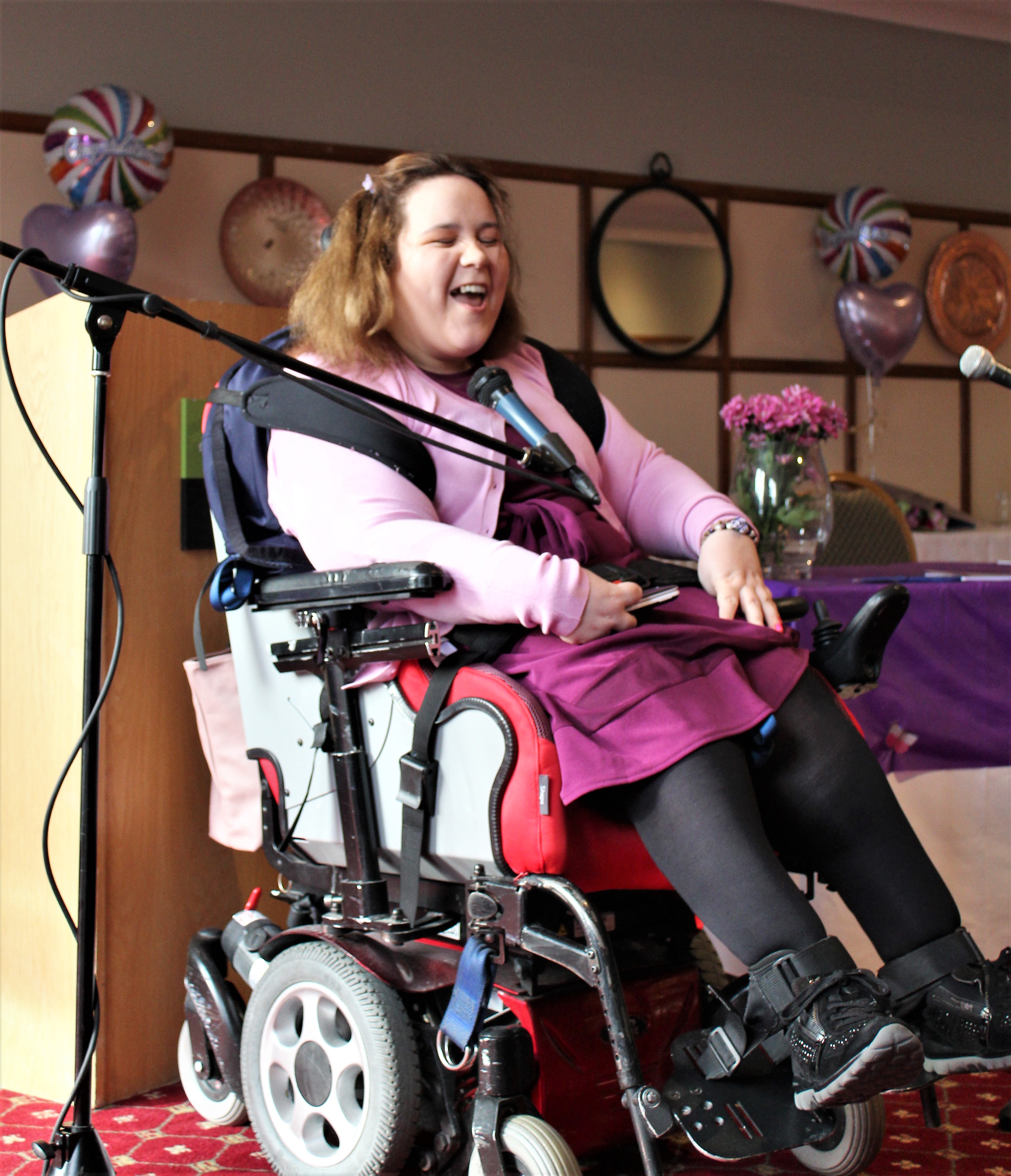 Image of a woman in a wheelchair speaking into a microphone