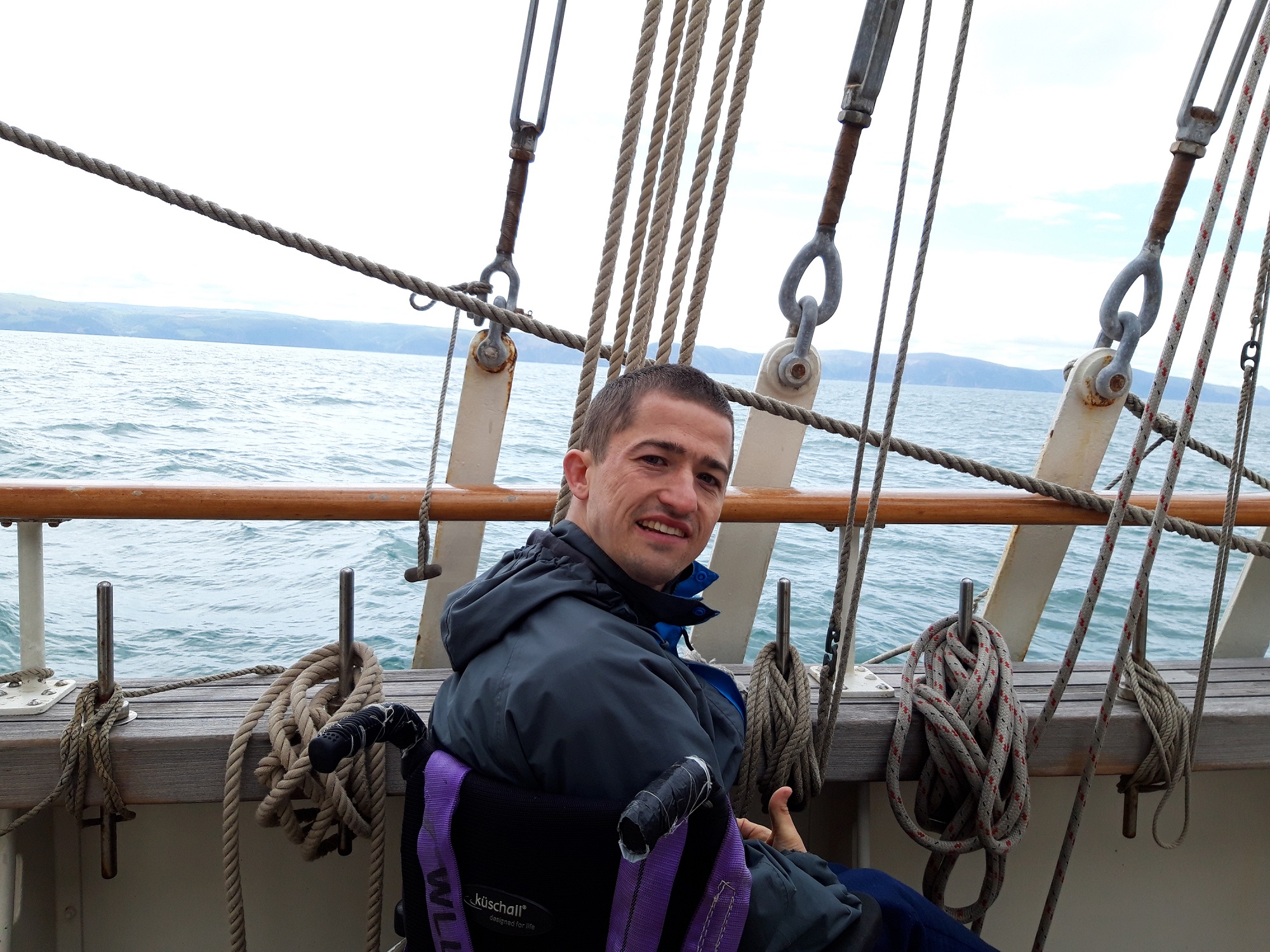 Young man using a wheelchair on board a tall ship with sea in the background