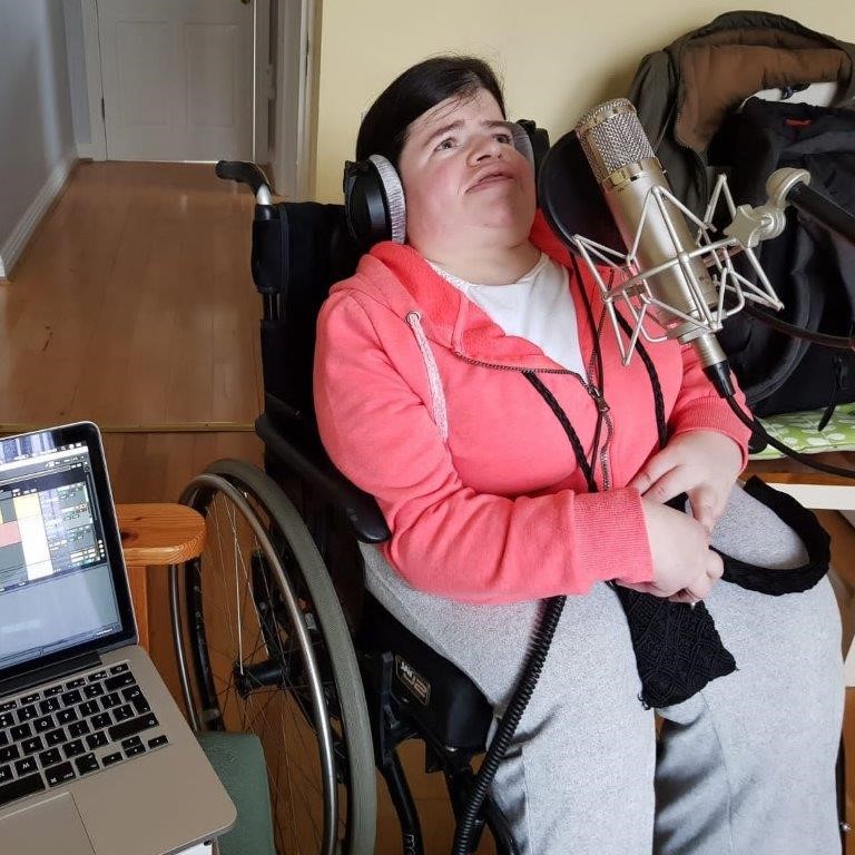 Woman using wheelchair sings into a microphone