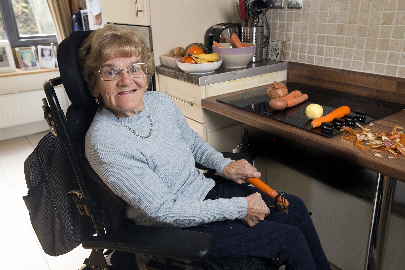 Woman using a wheelchair and peeling vegetables in her kitchen