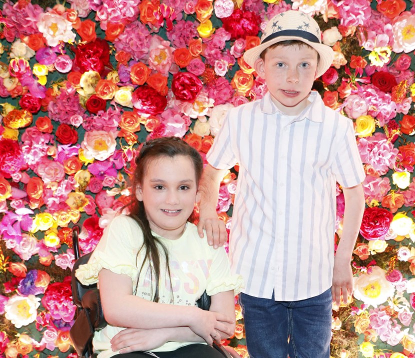 Girl and boy in front of wall of roses at a fashion show
