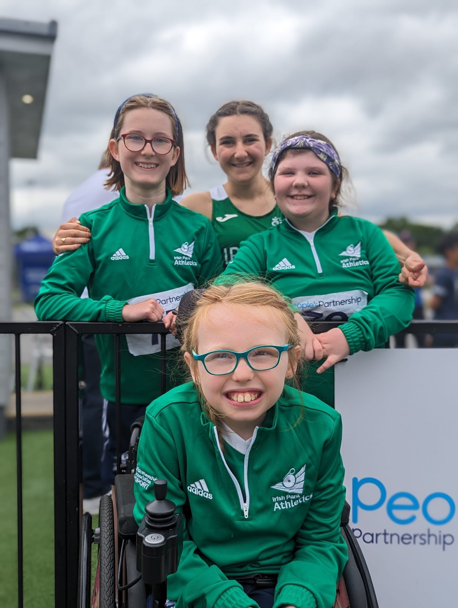 A photo of four girls in a green athletics track suits smiling at the camera.