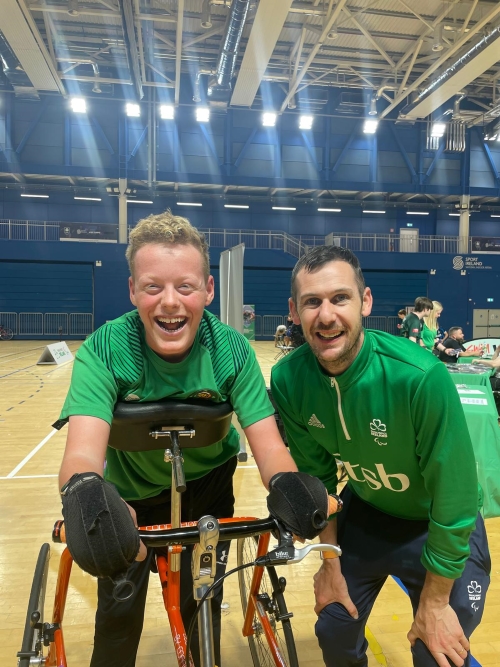 A photo of a teenage boy on a frame runner bike next to a man in a Paralympics Ireland jersey.