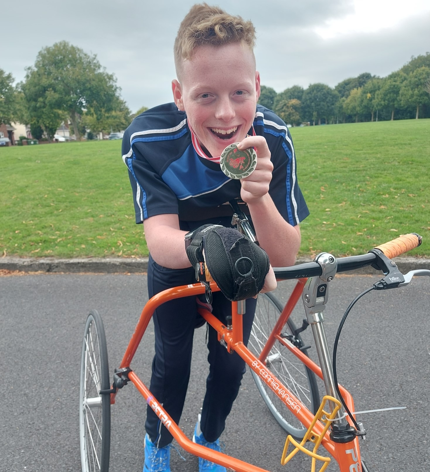 A teenage boy outdoors on a frame runner holding a silver medal