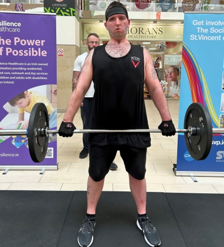 A photo of a man lifting a weight bar in a shopping mall.