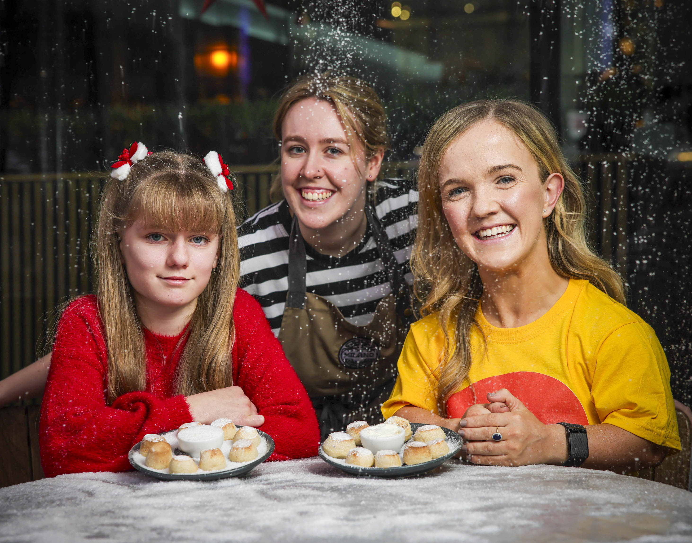 Smiling girl and two young women holding a place of dough balls with snow falling