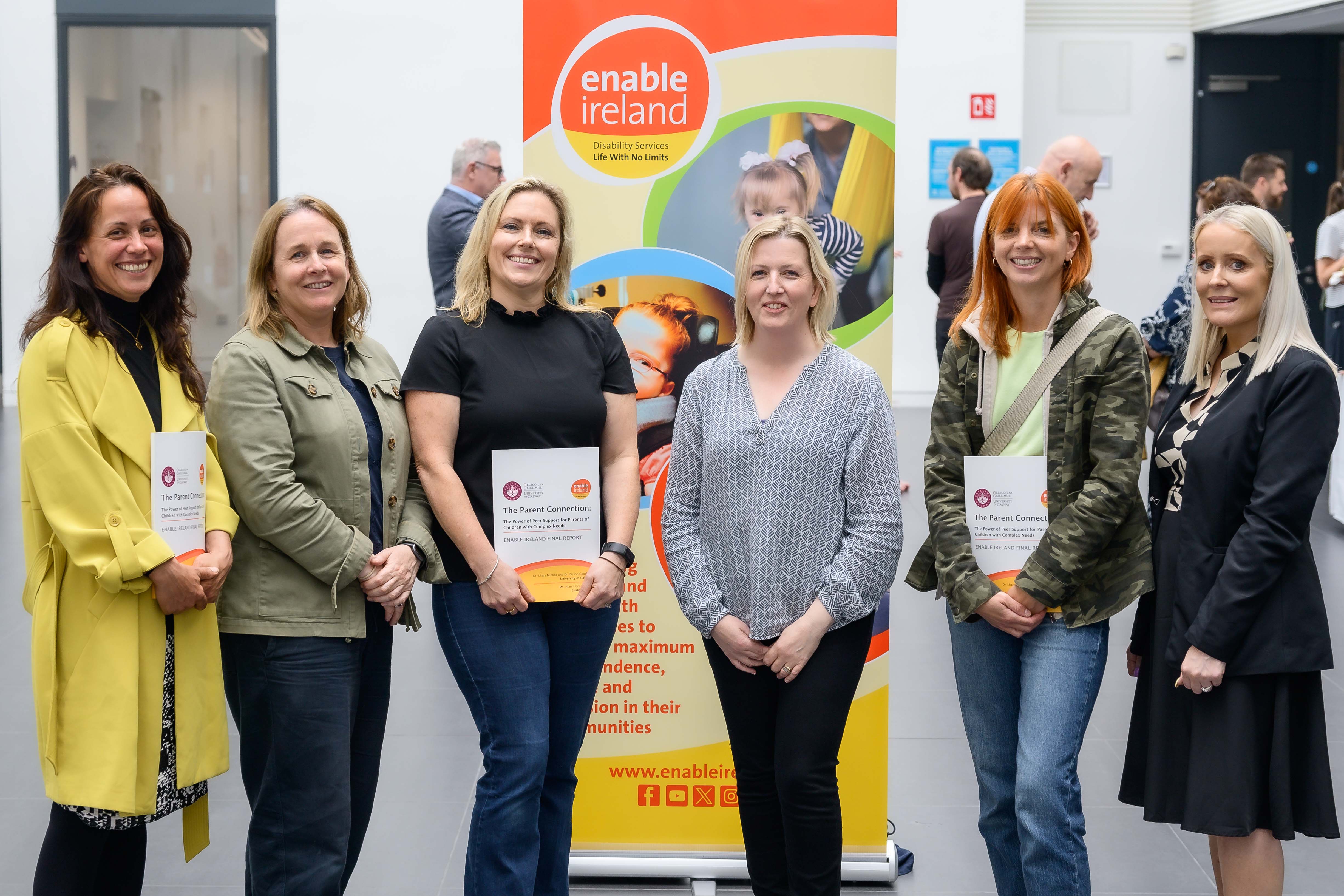 Six women stand in from of a colourful pop up banner holding copies of the newly published Parent Connection Report