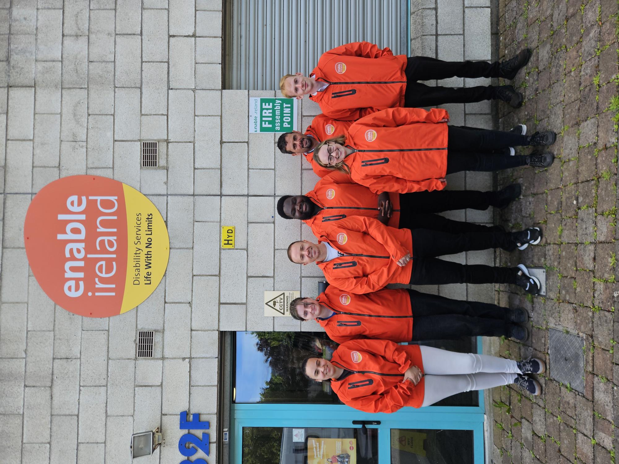 Enable Ireland's Face-to-Face fundraising team standing together outside the Enable Ireland Headquarters in orange Enable Ireland jackets