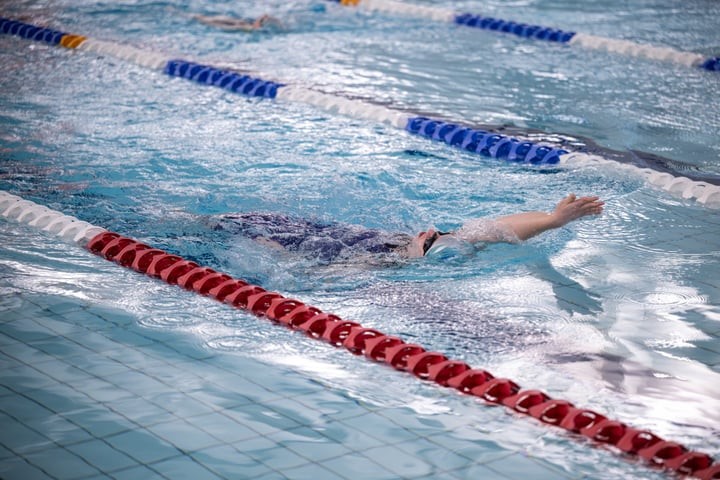 Photo of a girl swimming backstroke in the swimming lane of an indoor pool.