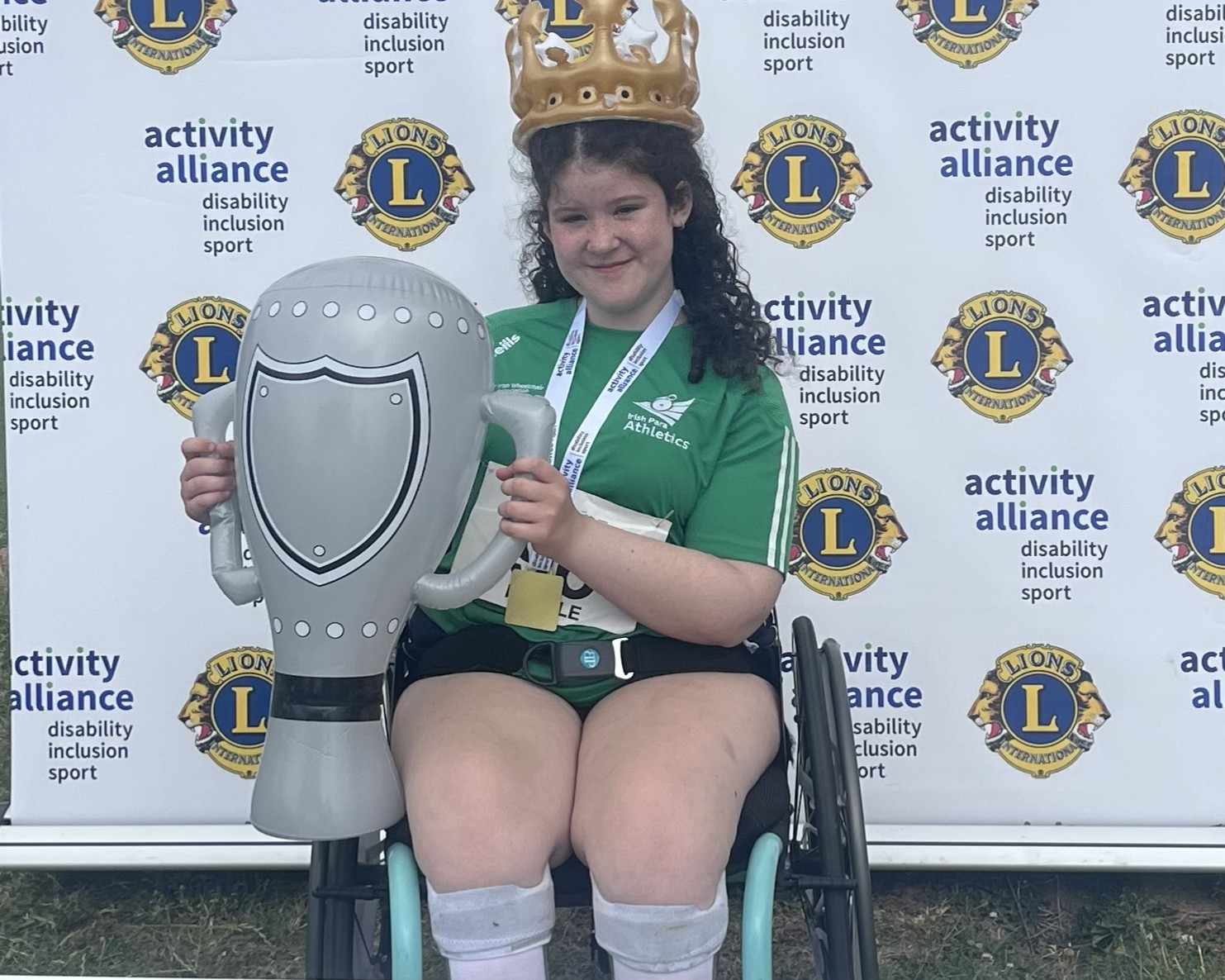Life With No Limits Champion Maisie Randle holding a large inflatable trophy while seated in a wheelchair at the activity alliance athletics event. The image features Activity Alliance and Lions International branding and highlights Maisie’s achievement as an international gold medalist.