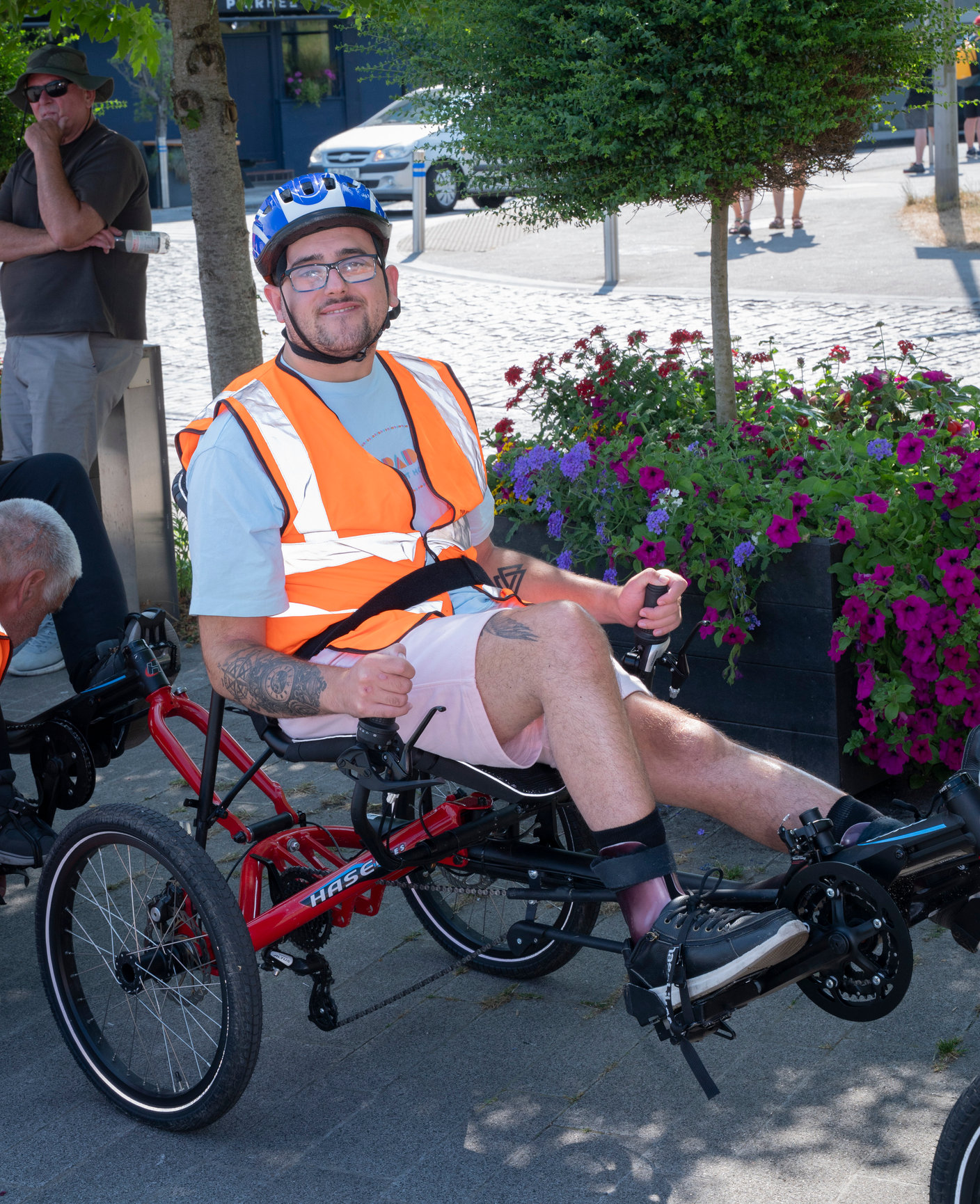 Life With No Limits Champion Jack participating in an inclusive cycling event on an adapted recumbent bicycle, wearing a helmet and high‑visibility vest in an outdoor community setting.