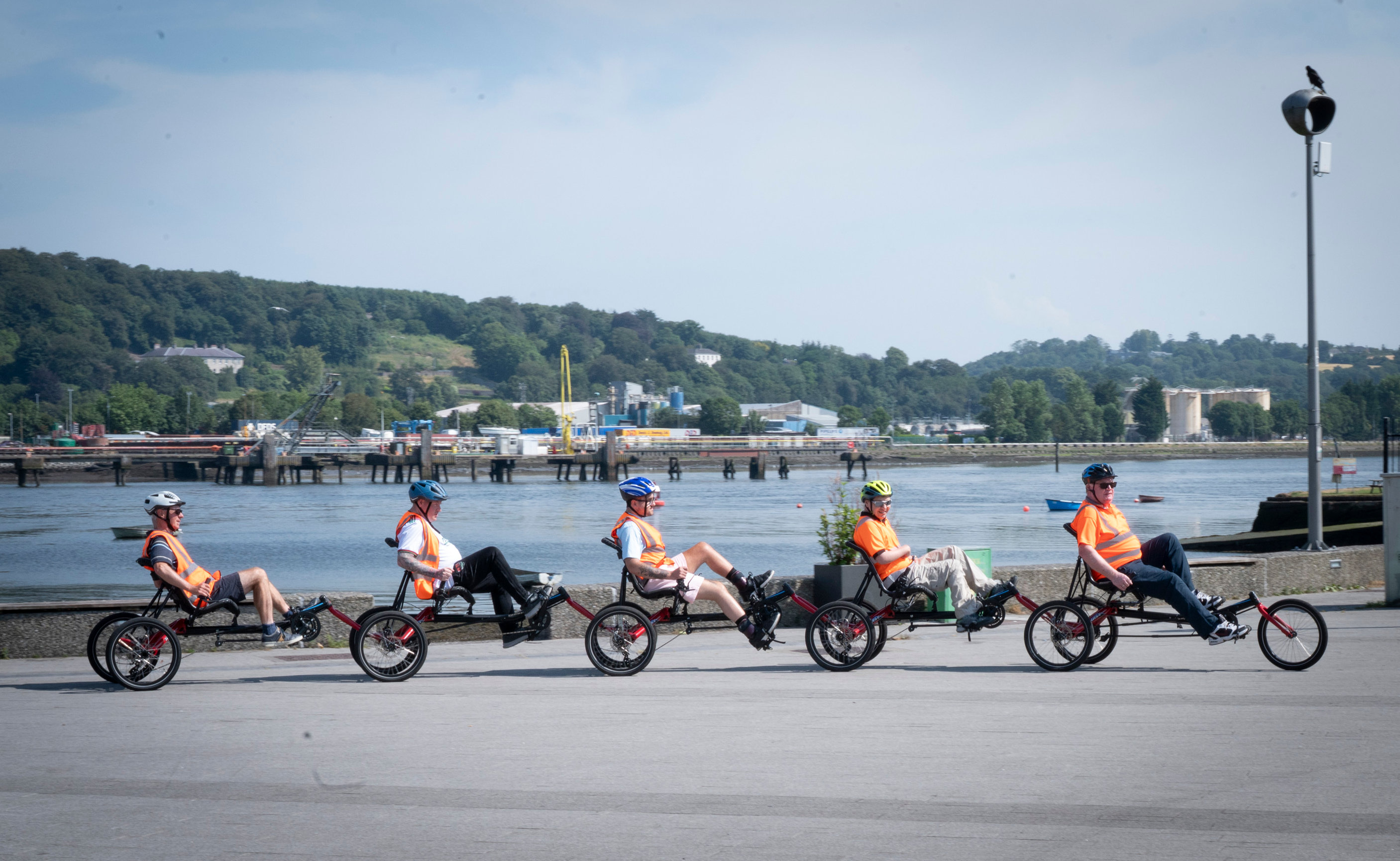 Life With No Limits Champions taking part in an inclusive cycling event on adapted recumbent bicycles along a waterfront promenade. The image shows four cyclists travelling together beside a river, highlighting accessible sport, participation and community inclusion.