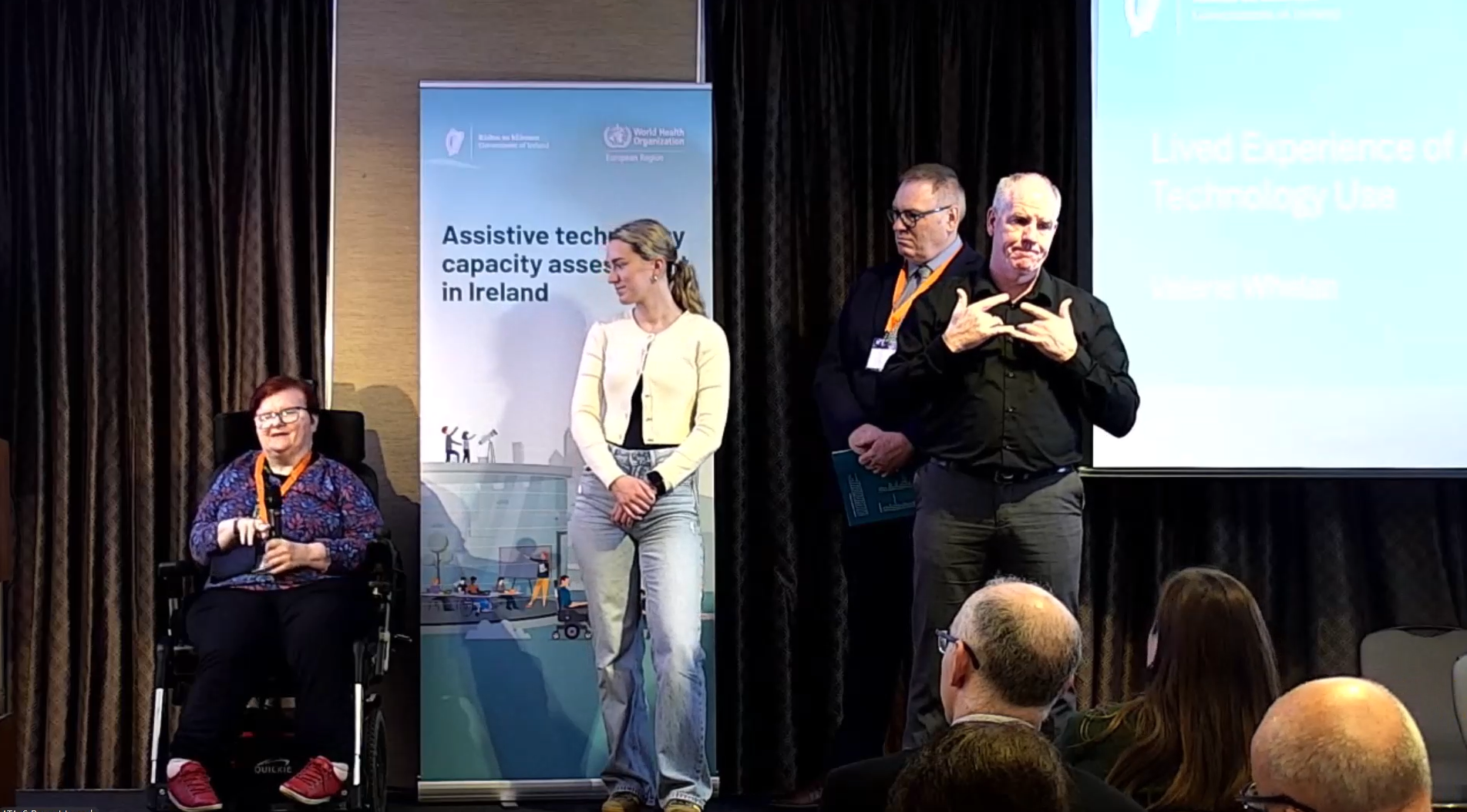 Assistive technology advocate delivering a presentation at the launch of Ireland’s Assistive Technology Capacity Assessment report, with a sign language interpreter, event speakers and audience members visible in a conference setting.