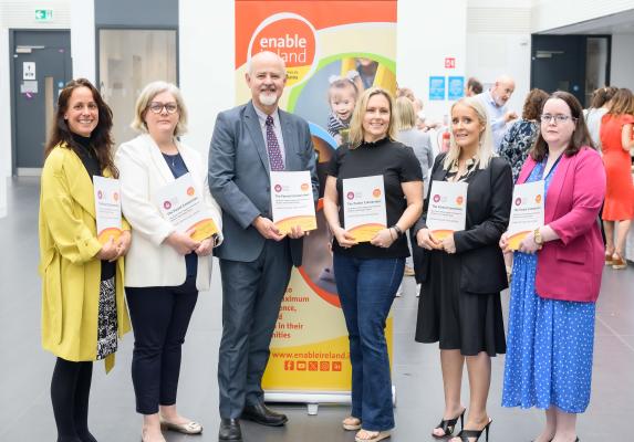 Five woman and one man stand in front of a colourful pop up banner holding copies of the Parent Connection Report. 