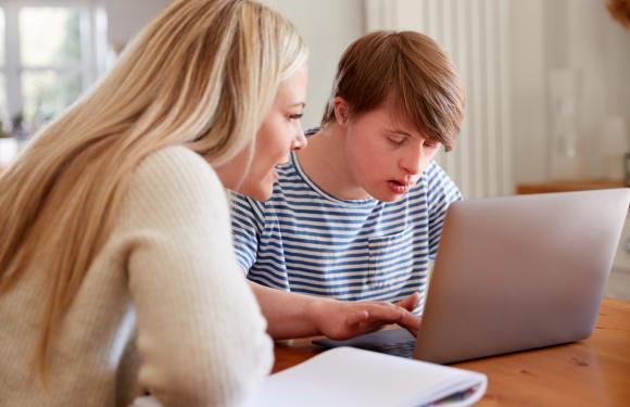 Woman works with a teenage boy on laptop
