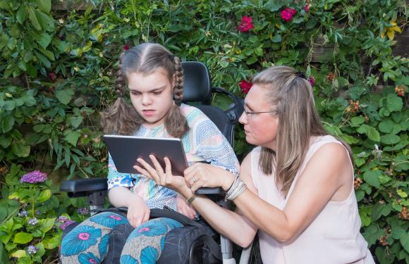 Staff member shows a tablet to a young wheelchair user