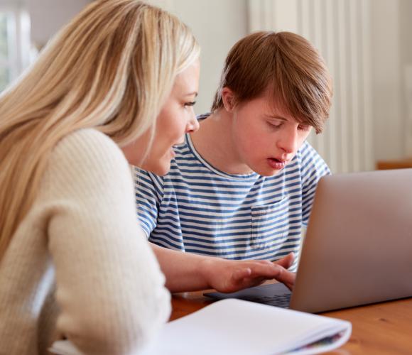 Woman sitting beside a young person using a laptop