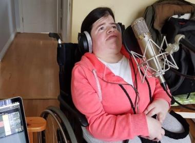 Woman using a wheelchair sings into a microphone