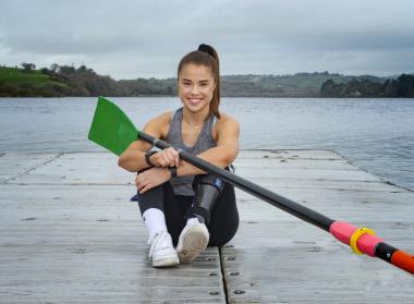 Woman sits beside water on a dock holding an oar
