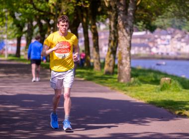 A man in a yellow Enable Ireland t-shirt running next to trees by a river bank.