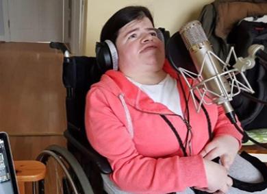 Woman using a wheelchair sings into a microphone