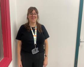 Woman wearing a black top and trousers standing against a white wall