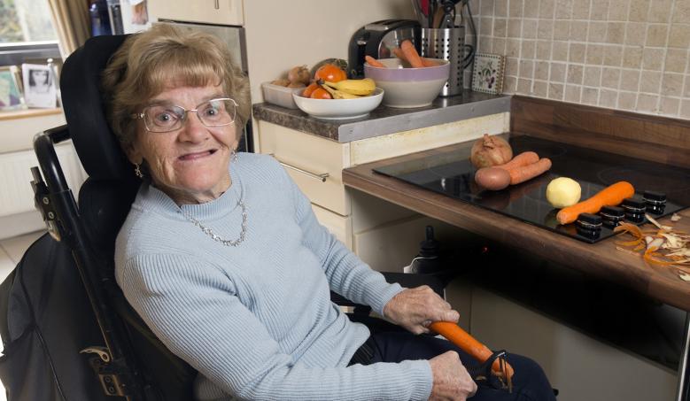 Woman in a wheelchair in her kitchen peeling carrots